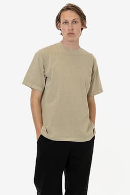 A short sleeve garment dye crewneck tee in a muted beige colour, worn by a model with hands in pockets.
