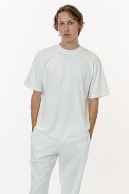 A white short sleeve garment dye crewneck tee, styled with a relaxed fit, shown on a model with matching trousers.