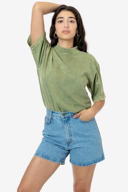 A model wearing a green mineral wash short sleeve crew tee paired with blue denim shorts, with a logo visible on the tee.
