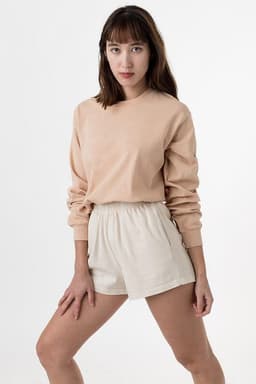 A long sleeve crewneck tee in peach, paired with light beige shorts, displayed on a model against a neutral backdrop.