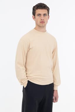 A long sleeve crewneck tee in beige, featuring a fitted design and a logo on the garment.