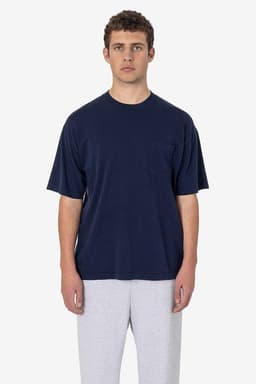 A model wearing a navy short sleeve garment-dyed pocket tee paired with grey sweatpants. The shirt features a pocket and has a logo.