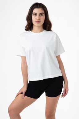A model wearing a white wide tee shirt paired with black shorts, standing against a plain background.