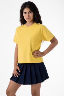A woman stands wearing a yellow garment dye wide tee and a navy pleated skirt, showcasing the shirt's relaxed fit.