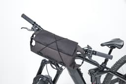 A black bicycle handlebar bag secured to a bike's handlebars, featuring a sleek design and straps for attachment.