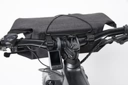 A grey bicycle handlebar bag rests on the handlebars, with a device attached and a logo visible.