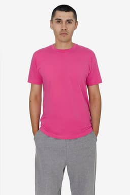 A model wearing a pink short sleeve fine jersey crew tee paired with grey trousers. The tee features a logo.