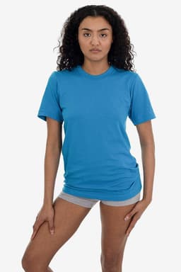 A woman poses in a blue short sleeve fine jersey crew tee, paired with grey shorts. The shirt has a logo.