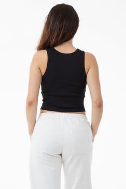 A woman is wearing a black 2x1 rib crop tank top, viewed from the back, paired with white pants.