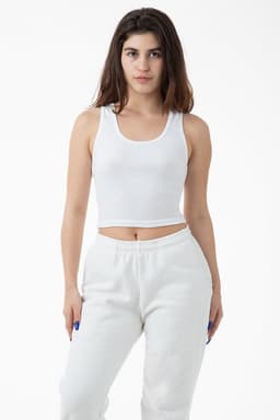 A cropped tank top in white, featuring a fitted design and a round neckline. The model pairs it with white sweatpants.