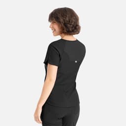 A woman is wearing a black Embrace Luna Tuckable Y-Neck Top, viewed from the back. The top features a logo.