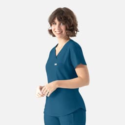 A woman wearing a teal Y-neck top with a pocket, featuring a logo on the chest.