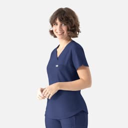 A woman wearing a navy blue Y-neck top with a pocket and a logo. She has short, curly hair and is smiling.