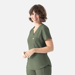 A woman in a green Y-neck top with a pocket and branding appears against a neutral background.