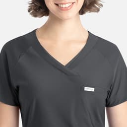 A dark grey Y-neck top featuring a tucked design and a small pocket, modelled by a smiling person with short hair.