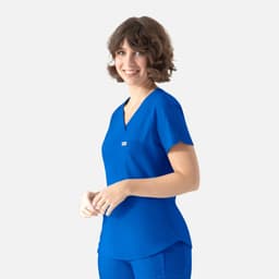 A woman models a blue scrub top with a V-neck and a small pocket. It features a branding logo.