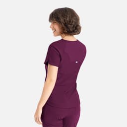 A woman is wearing a purple Embrace Luna Tuckable Y-Neck Top, viewed from the back. The top features a logo.