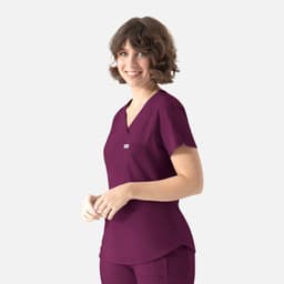 A woman wears a plum-coloured Y-neck top with short sleeves, featuring a small logo on the chest.