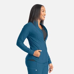 A woman smiles while wearing a teal full zip track jacket, featuring a fitted design and a logo on the side.