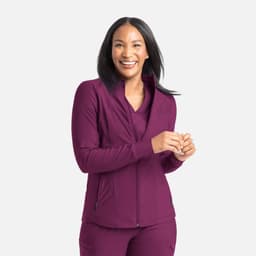 A woman wearing a full zip track jacket in a rich plum colour, smiling and standing against a neutral background.