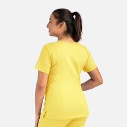A woman in a bright yellow double V-neck top, showcased from the back, with a ponytail hairstyle.