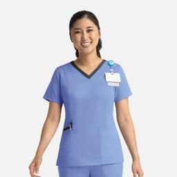 A nurse in a blue scrub top with a contrast V-neck and pocket details, wearing a badge and a smile.