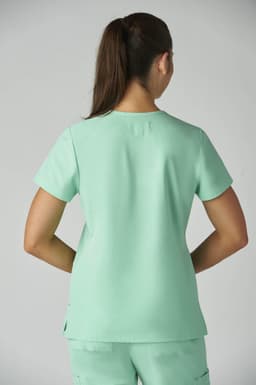 A woman is wearing a light mint green Becca Top, viewed from the back, with short sleeves and a relaxed fit.