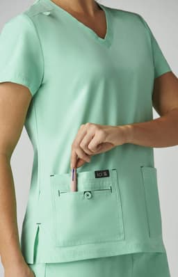 A mint green medical top with short sleeves and two front pockets, featuring a logo on one pocket.