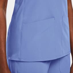 A women's mock wrap top in light blue, featuring two front pockets and a smooth fabric. It has a logo displayed.