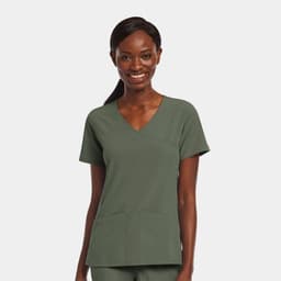 A woman smiles while wearing a green mock wrap top with two front pockets, featuring a logo.