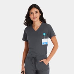 A woman in a grey V-neck top with a badge and logo, featuring a tuckable design.