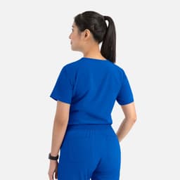 A woman in a vibrant blue tuckable V-neck top and matching bottoms, viewed from the back. The outfit features a logo.