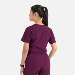 A woman wearing a purple women's tuckable V-neck top, viewed from the back, with a logo visible on the top.
