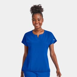 A woman wearing a bright blue notched neck dolman top, smiling confidently with a simple design and a logo.