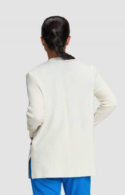 A woman stands with her back to the camera, wearing a white Kori Sweater and blue pants.