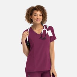 A woman in a plum-coloured mock wrap top, wearing a stethoscope around her neck, with a logo visible.