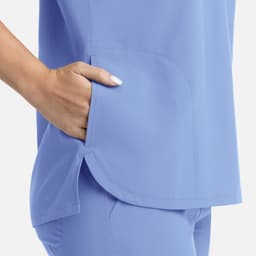 A light blue women's top featuring a dolman sleeve design and three pockets. It has a logo on it.