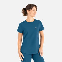 A woman wearing a teal round neck scrub top with a pocket and a logo, styled for uniforms.