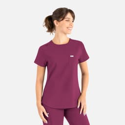 A scrub top in a rich plum colour with a pocket and branding, worn by a smiling model.