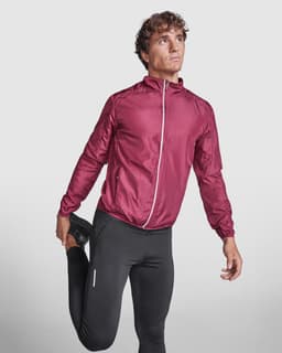 A model wearing a burgundy lightweight windbreaker, paired with black athletic pants, in a stretching pose.