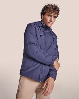 A water-repellent jacket in navy blue, featuring a hood and zip closure, modelled by a person.