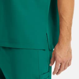 A close-up of a men's tuckable v-neck top in teal, featuring a side slit and a hand resting on the fabric.