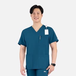 A man wearing a teal V-neck top featuring four pockets and a logo, smiling against a plain background.