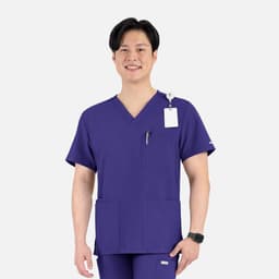 A purple V-neck top with four pockets, featuring a logo, worn by a smiling man.