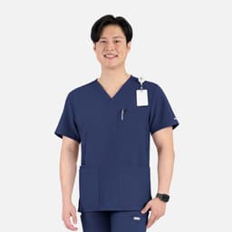 A navy V-neck top with four pockets, featuring a logo and a tag, worn by a smiling male model.
