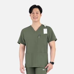 A man wearing a green V-neck top with four pockets, featuring a logo and a tag on the shoulder.