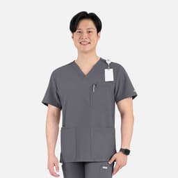 A man wearing a grey V-neck top with four pockets, featuring a logo on the left side.