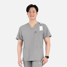 A grey V-neck top with four pockets, worn by a smiling man. The top features a logo and tag.