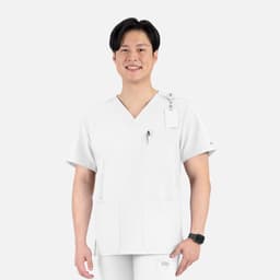 A man in a white V-neck top featuring four pockets and a logo, smiling against a plain background.
