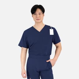 A man wearing a navy blue V-neck top with short sleeves and a pocket. The top has a tag attached.